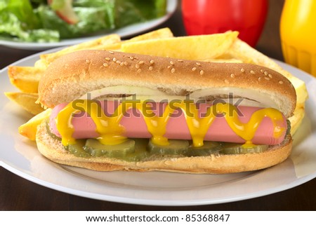 Hotdog with pickles, onion and mustard served with French fries (Selective Focus, Focus on the front of the sausage)