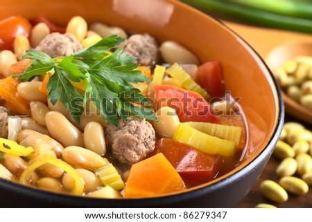 Canary bean soup with meatballs and vegetables, such as leek, tomato, carrot and potato (Selective Focus, Focus on the front of the meatball and the front edges of the parsley)