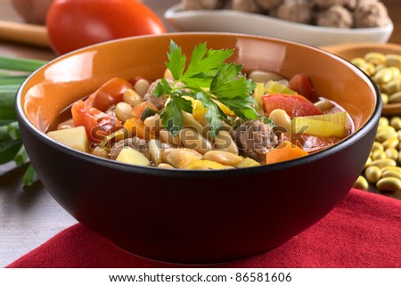Canary bean soup with meatballs and other vegetables garnished with a parsley leaf (Selective Focus, Focus on the meatball in the front)