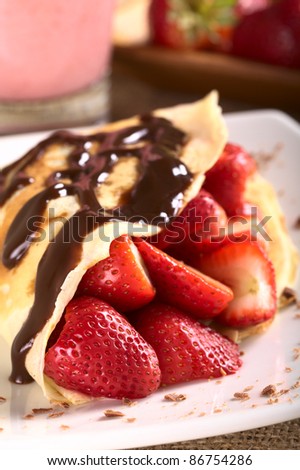 Crepe filled with fresh strawberries and chocolate sauce on top garnished with chocolate shavings on the plate (Selective Focus, Focus on the strawberry in the front)