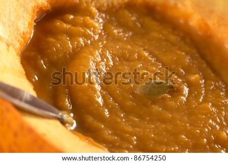 Fresh creamy pumpkin soup served in a pumpkin with a spoon and garnished with a pumpkin seed (Selective Focus, Focus on the seed)