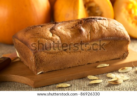 Fresh baked pumpkin bread on wooden board with pumpkin seeds and pumpkins (Selective Focus, Focus on the left front of the bread)