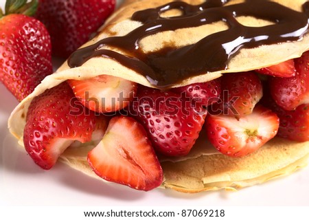 Crepe filled with fresh strawberries and chocolate sauce on top (Selective Focus, Focus on the strawberry cut on the left and the front of the two strawberries beside)