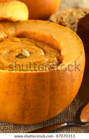 Fresh creamy pumpkin soup served in a pumpkin and garnished with pumpkin seeds (Selective Focus, Focus on the seeds)