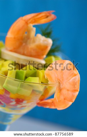 King prawn on the rim of a cocktail glass containing a salad of onion, pepper, mango and avocado, calamari, king prawn and dill (Selective Focus, Focus on the right side of the prawn on the glass rim)