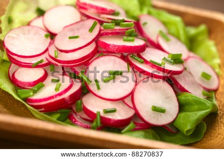 Fresh radish salad with chives served on a lettuce leaf on a wooden bowl (Selective Focus, Focus in the middle of the photo)