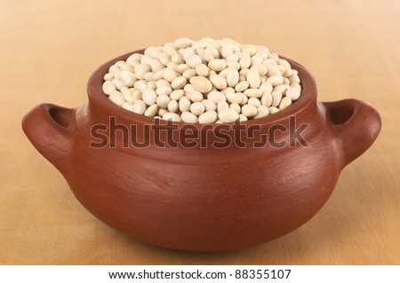 Raw navy beans (haricot beans, Boston beans, pea beans, Yankee beans) in rustic bowl photographed on wood (Selective Focus, Focus on the beans in the front of the bowl)