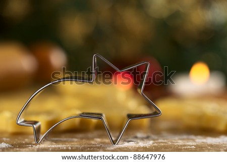Shooting star shaped cookie cutter with raw cookies and Christmas decoration in the back (Selective Focus, Focus on the front edge of the cutter)