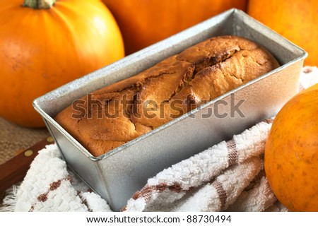 Fresh baked pumpkin bread in baking form with pumpkins around (Selective Focus, Focus one third into the bread on the left side)