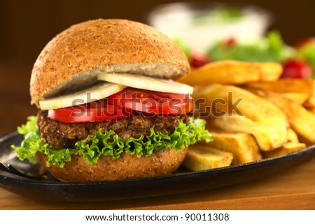 Vegetarian lentil burger in wholewheat bun with lettuce, tomato and cucumber accompanied by French fries (Selective Focus, Focus on the front of the sandwich)
