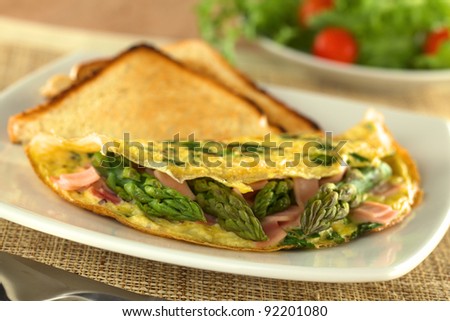 Green asparagus and ham omelet with toast bread and a fresh salad in the back (Selective Focus, Focus on the three asparagus tips in the front)