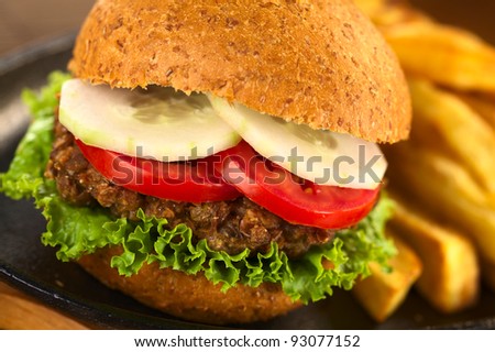 Vegetarian lentil burger in wholewheat bun with lettuce, tomato and cucumber accompanied by French fries (Selective Focus, Focus on the front of the lettuce, lentil burger, tomato and cucumber)