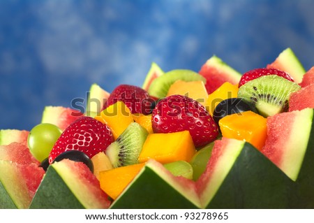 Fresh fruit salad of mango, strawberry, kiwi and grapes in a bowl from watermelon in front of blue background (Selective Focus, Focus in the middle of the fruit salad)