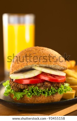 Vegetarian lentil burger in wholewheat bun with lettuce, tomato and cucumber accompanied by French fries and orange juice (Selective Focus, Focus on the front of the sandwich)