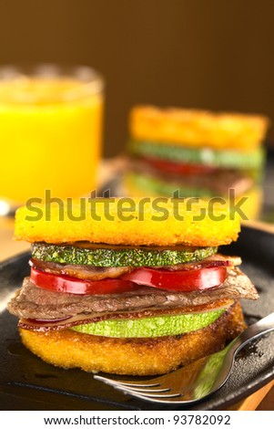 Polenta burgers with fried zucchini, bacon, beef and tomato accompanied by orange juice (Selective Focus, Focus on the front of the burger)