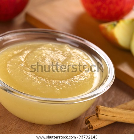 Fresh homemade apple sauce with cinnamon sticks on the side and apple in the back (Selective Focus, Focus one third into the apple sauce)