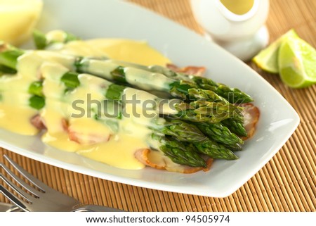 Cooked green asparagus on fried bacon with Hollandaise sauce on top (Selective Focus, Focus on the five asparagus tips in the front)