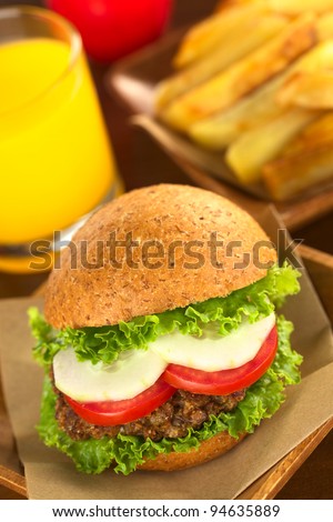 Vegetarian lentil burger in wholewheat bun with lettuce, tomato and cucumber accompanied by French fries and orange juice (Selective Focus, Focus on the front of the sandwich)
