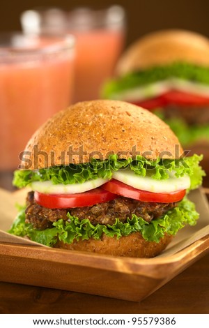 Vegetarian lentil burgers in wholewheat bun with lettuce, tomato and cucumber accompanied by camu camu juice (Selective Focus, Focus on the front of the sandwich)