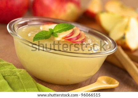 Fresh homemade apple sauce with apples in the back (Selective Focus, Focus on the front of the apple slices and the mint leaf on the sauce)