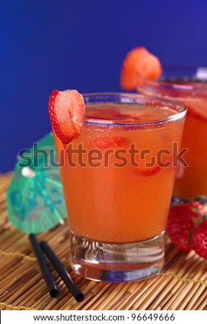 Peruvian cocktail called Pisquina made of pisco, passionfruit and cranberry juice, strawberries, sugar, ice (Selective Focus, Focus on the front rim of the glass and the front of the strawberry slice)
