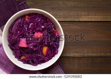 Braised red cabbage with apple in bowl, photographed overhead on dark wood with natural light (Selective Focus, Focus on the top of the dish)