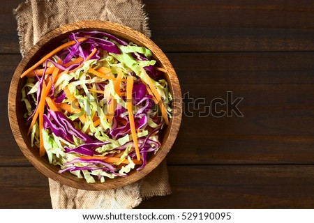 Fresh coleslaw salad made of shredded red and white cabbage and carrots, served in wooden bowl, photographed overhead on dark wood with natural light (Selective Focus, Focus on the top of the salad)
