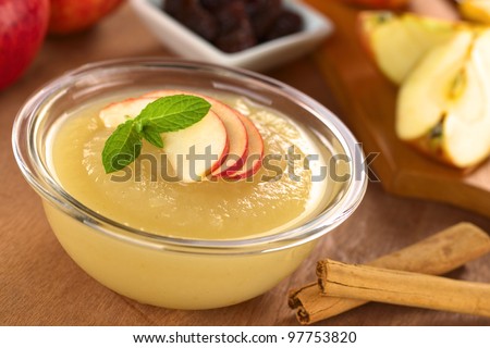 Fresh homemade apple sauce with cinnamon sticks on the side, apple and raisins in the back (Selective Focus, Focus on the front of the apple slices on the sauce)
