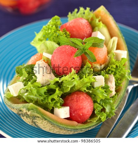 Fresh salad made of watermelon, cantaloupe melon, chicken, cucumber, cheese and lettuce (Selective Focus, Focus on the front of the mint leaf and the watermelon ball below it)