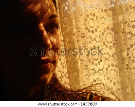 Woman looking through a window with curtain shadow falling onto her face