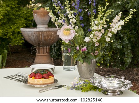 Dessert table in outdoor garden, fruit dessert, bouquet, and fountain in the background