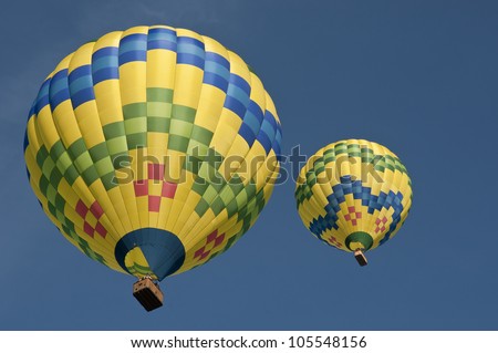 Looking up at two hot air balloons with opposite color patterns, clear blue skies, large baskets