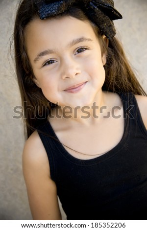 Very cute six year old brunette girl looking up at camera, shy little smile, ribbon in hair