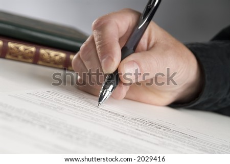 man\'s hand holding a pen writing,books in background