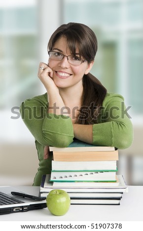 young woman looking like a student/teacher, with laptop, stack of books,green apple