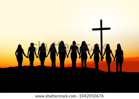 Sunset silhouette of 10 young women walking hand in hand toward a Christian Cross.
