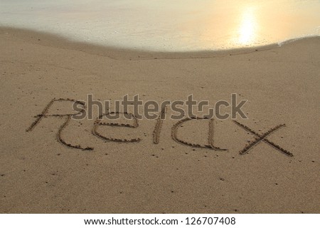 The word relax hand written in the sand at sunset.
