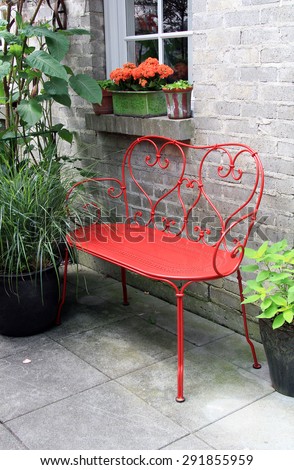 Red wrought iron bench outside on a garden patio.