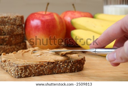Making lunch, peanut butter sandwich. Apples, bananas and a glass of milk in the background.