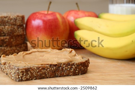 Peanut butter sandwich, apples, bananas and a glass of milk in the background.