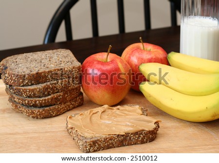Peanut butter sandwich, apples, bananas and milk in the background.