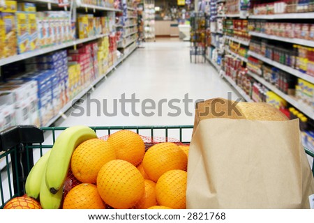Grocery cart loaded with fresh fruit and bread moving through the aisle.