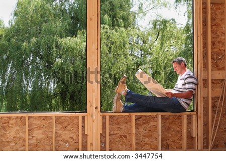 Man relaxed and reading the blue prints of his new home still under construction.