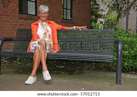 Seventy year old friendly lady seated on a park bench.