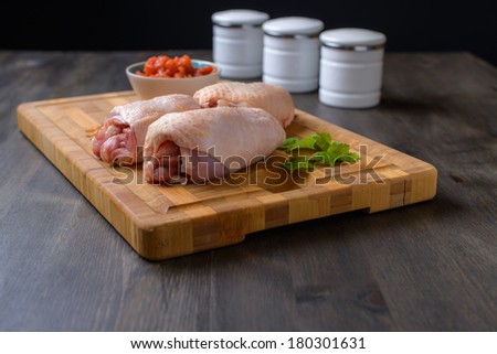 Raw chicken on a cutting board with some salsa and greens