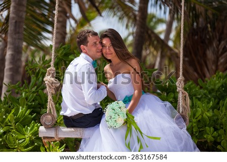 young loving couple on their wedding day, on the swing, outdoor beach wedding in tropics