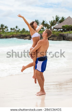 Guy holds girl on hands. Ocean beach.
