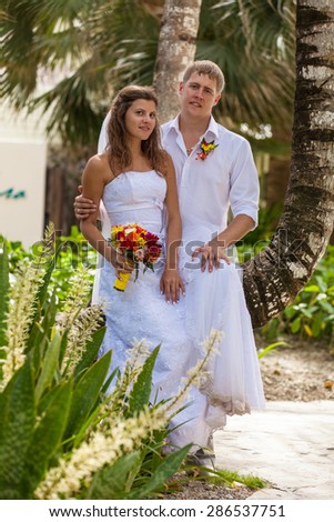 bride and groom on the background of palm trees. happy newlywed couple holding hands and flower