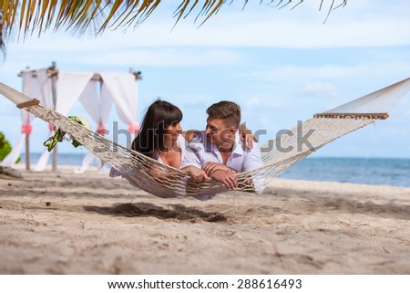 young loving couple on their wedding day, relaxing in beach hammock, outdoor beach wedding in tropics