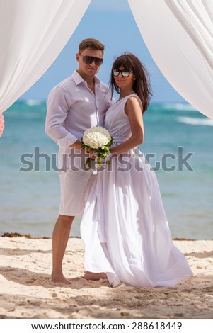 young loving couple on their wedding day, beautiful wedding arch on beach, outdoor beach wedding in tropics